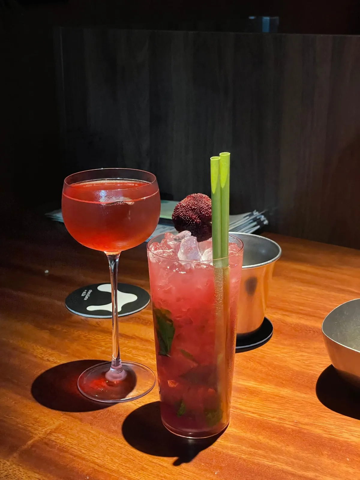 A red cocktail in a coupe beside a tall glass of crushed ice and mint topped with a waxberry, at Chocolate+Milk